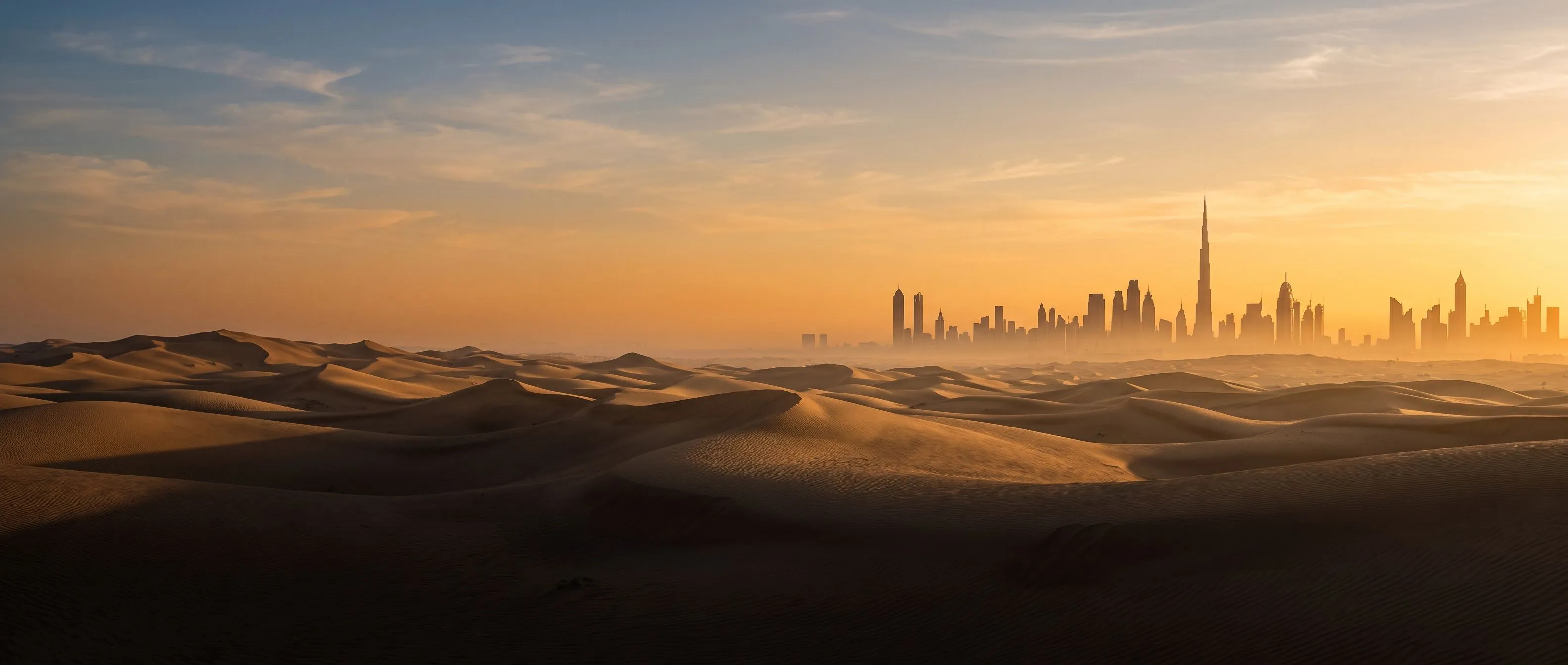 Desert dunes meeting the Dubai skyline at sunrise